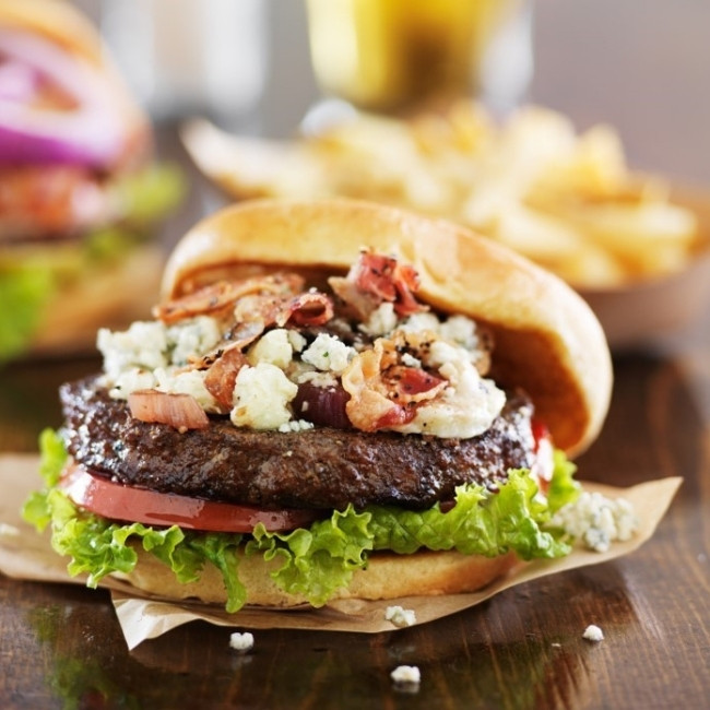 Close-up of a gourmet burger from the Food Menu Dilworth MN, with fries in the background.