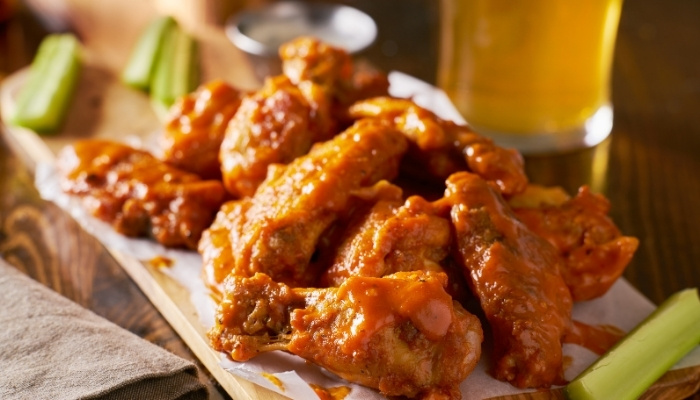 Buffalo chicken wings with sauce at Silver Spike Bar & Grill, served with celery and a drink.