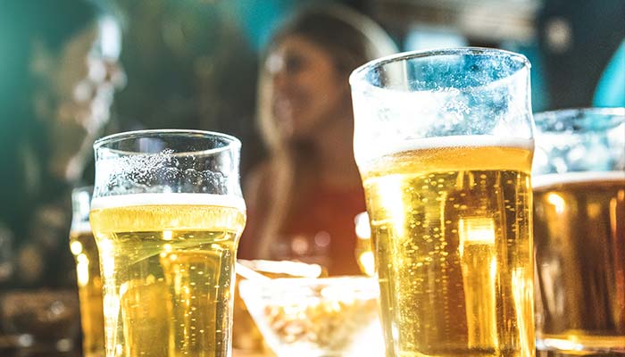 Glasses of beer on a table at Bar & Drinks Dilworth MN, with friends socializing nearby.